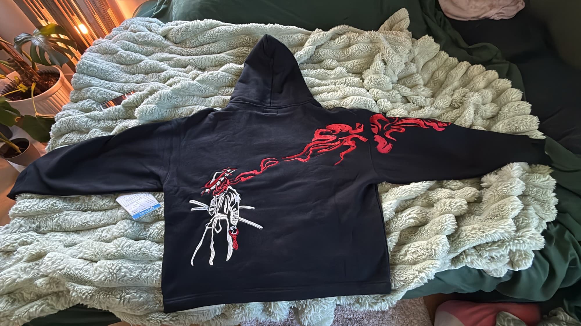 Keeshee hoodie laid flat, back view, with an embroidered samurai and red flames running down the sleeve